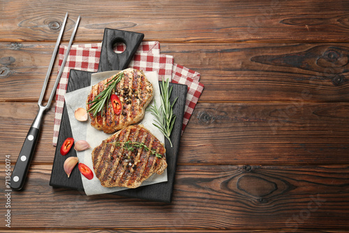 Delicious grilled pork steaks with spices and meat fork on wooden table, top view. Space for text