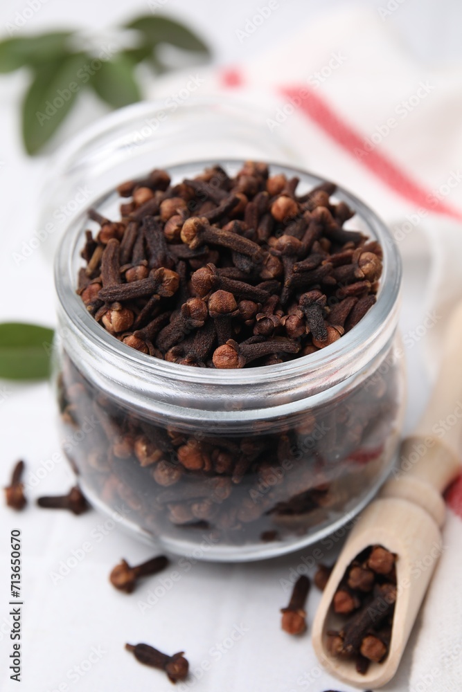 Aromatic cloves in glass jar and scoop on white table, closeup Aromatic cloves in glass jar and scoop on white table, closeup