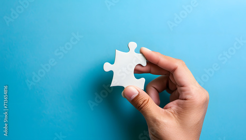 hand holding a jigsaw puzzle piece in front of a blue background 