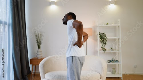 Unhappy black man suffering from pain in back or reins at home photo
