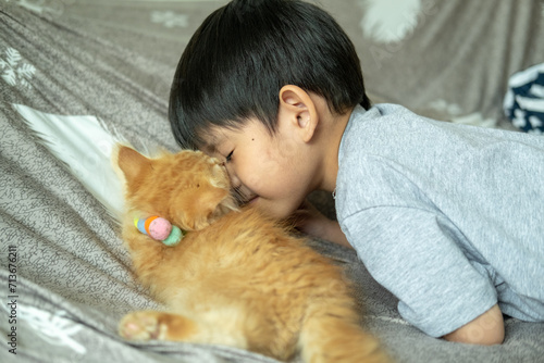 A little Asian boy kisses a small orange kitten.