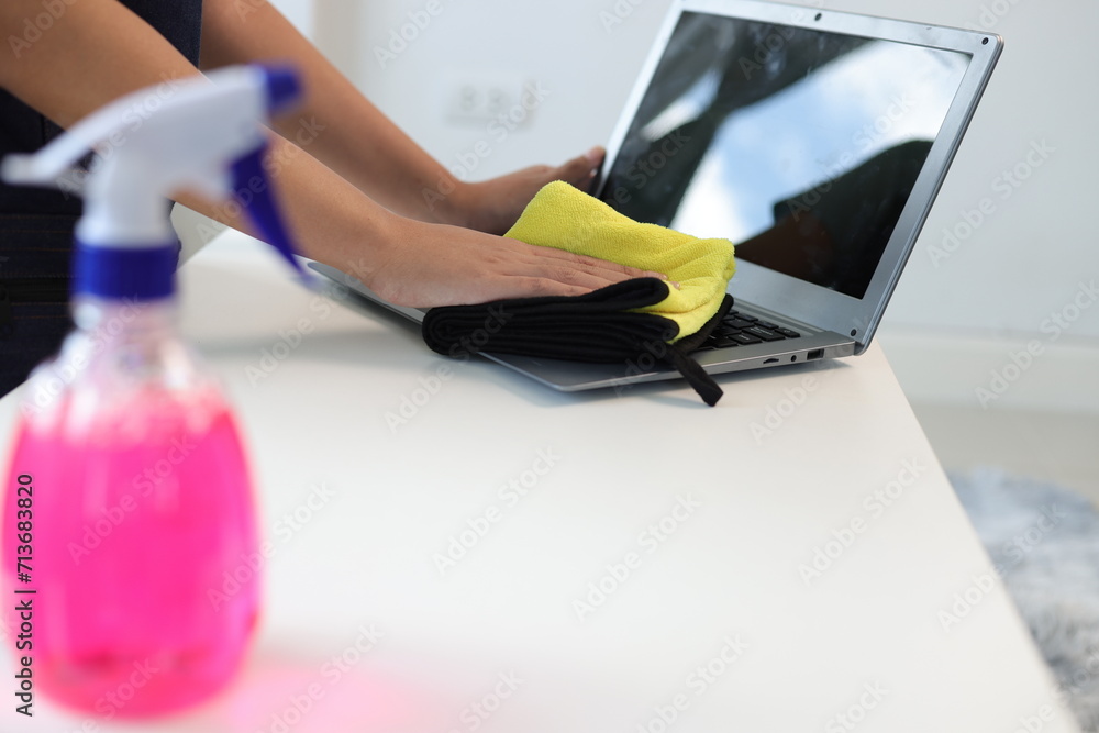 Young Asian cleaning woman uses a towel to clean a computer using cleaning solution in her home office.
