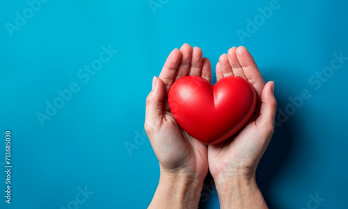 Hands cradling a red heart on a blue background