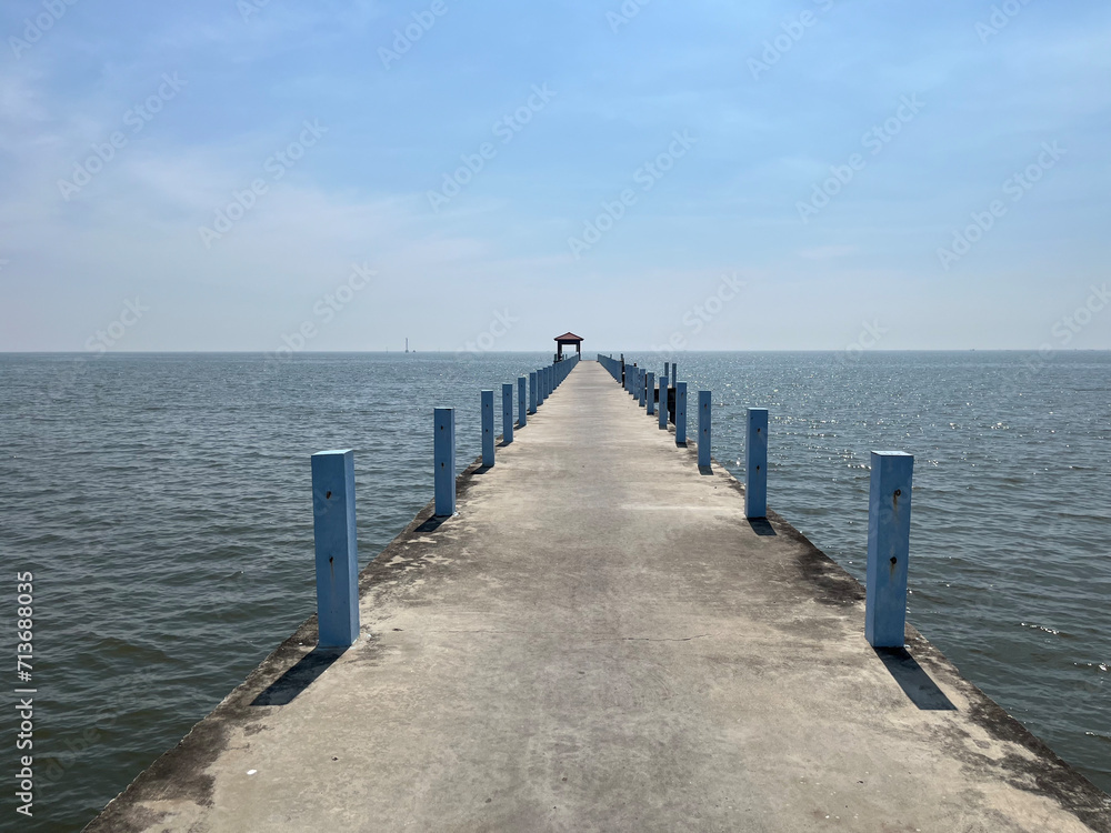 Photo of a cement bridge stretching into the sea with a pavilion at the end and a clear sky.