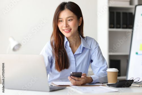 Asian woman in office is using mobile phone and calling someone, she is smiling with joy and surprise when receiving good news. © Kainnika