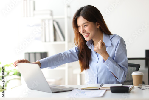 Asian woman in office is excited and happy while looking at surprise laptop screen.
