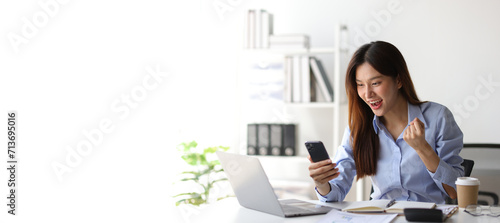 Asian woman in office is excited and happy while looking at surprise mobile phone screen.