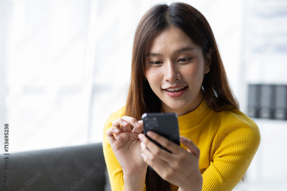 Happy young asian woman sitting on sofa using smartphone in living room at home. Happy young asian woman sitting on sofa using smartphone in living room at home.