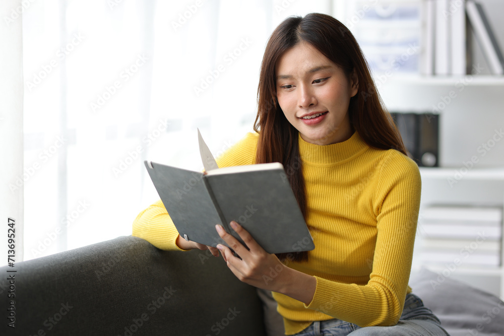 Charming Asian woman is happily reading a book on the sofa in the living room at home. Charming Asian woman is happily reading a book on the sofa in the living room at home.
