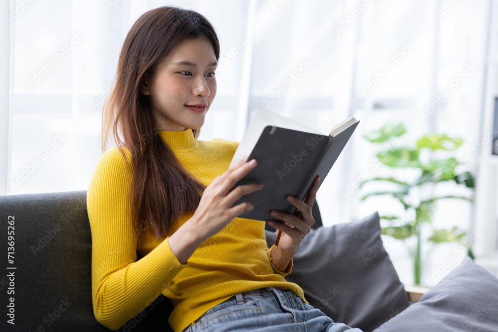 Charming Asian woman is happily reading a book on the sofa in the living room at home. Charming Asian woman is happily reading a book on the sofa in the living room at home.