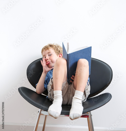 Silly boy sitting in a chair making a funny face while reading a book photo