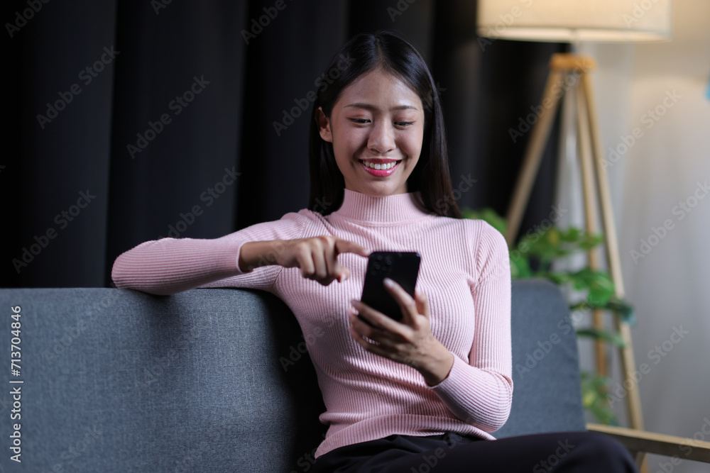 Young Asian woman sitting on sofa at home using mobile phone to send text messages and talk on the phone with her friends. Young Asian woman sitting on sofa at home using mobile phone to send text messages and talk on the phone with her friends.