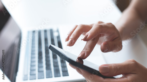 Close up of woman hand using mobile phone for online shopping and digital payment via mobile banking app. Business woman using smartphone while working on laptop computer on office table