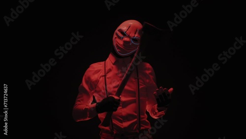 Portrait footage of a male actor wearing scary mask and holding ax and doing creepy moves photo