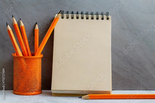 Notepad, orange pencils on the table. Mockup on office background for copy space. It is impo photo