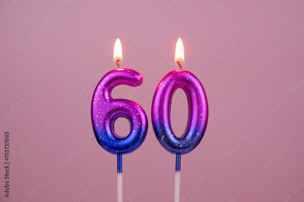 Pink and blue with white spots birthday candles burning on pink background. Number 60. Pink and blue with white spots birthday candles burning on pink background. Number 60.