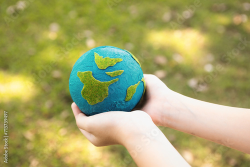 Fototapeta Naklejka Na Ścianę i Meble -  Young boy's hand holding planet Earth globe at natural park background as Earth day to save this planet with ESG principle and environment friendly energy for brighter future. Gyre