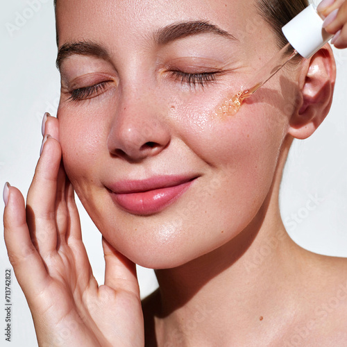 Moisturising and nourishing care serum. Close up beauty portrait of  young woman with glowing skin is applying a vitamin c skincare product with a pipette dropper. Facial hydration cosmetics