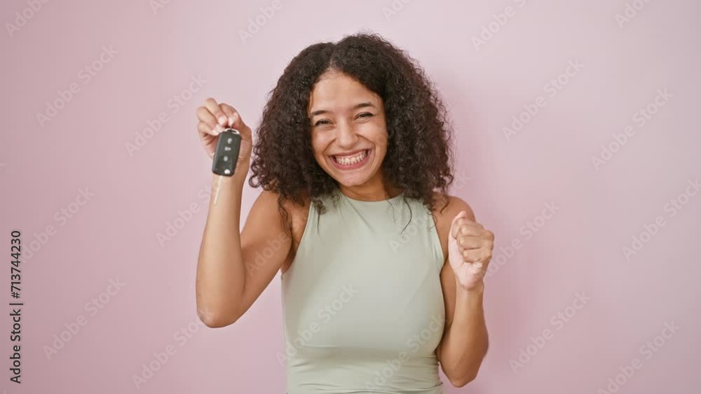 Overjoyed young hispanic woman, flashing a winner's smile, pointing at her new car key, celebrating her joyous win against a pink isolated background. Overjoyed young hispanic woman, flashing a winner's smile, pointing at her new car key, celebrating her joyous win against a pink isolated background.