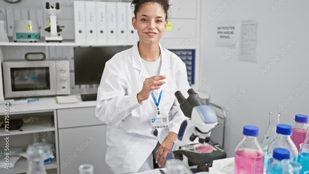 Confident young hispanic scientist, a beautiful woman with curly hair, smiling and making a crossed arms gesture while sitting at laboratory table, working with microscope in her medical research Confident young hispanic scientist, a beautiful woman with curly hair, smiling and making a crossed arms gesture while sitting at laboratory table, working with microscope in her medical research
