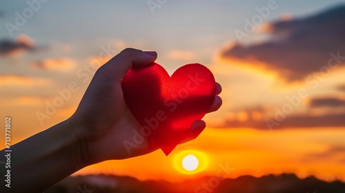In the warm glow of the sunset, a close-up of a hand holding a large red heart—an idea representing happiness, love, and the concept of Valentine's Day.