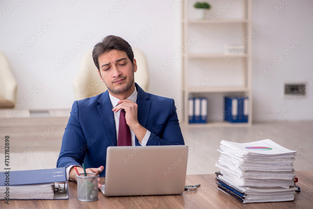 Young male employee unhappy with excessive work in the office Young male employee unhappy with excessive work in the office