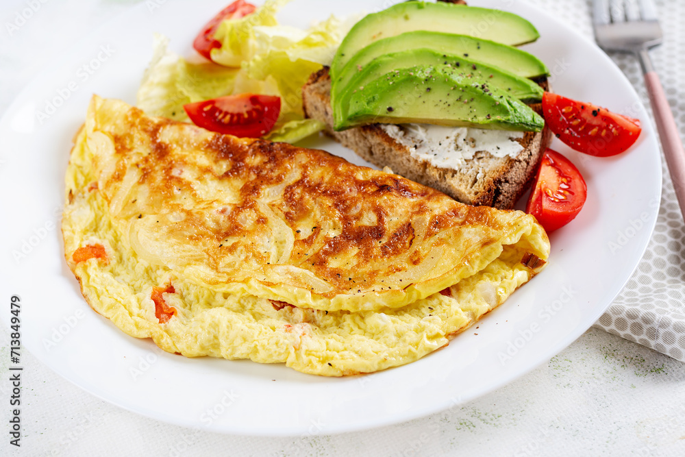 Omelette with tomatoes and toast with avocado on white plate. Frittata - italian omelet. Omelette with tomatoes and toast with avocado on white plate. Frittata - italian omelet.