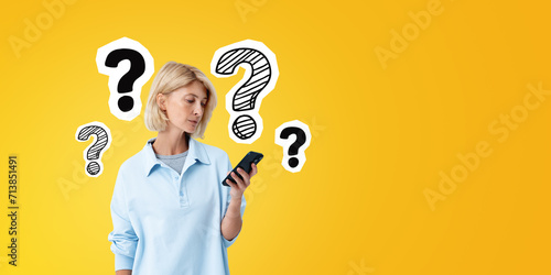 Young woman with phone in hand, question marks sketch on empty background photo