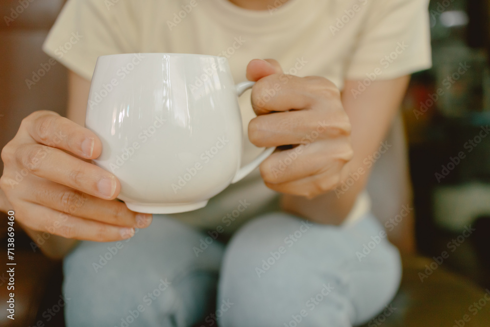 Close up of woman tow hands holding white coffee cup, showing milk tea glass while sitting on brown sofa at home. Close up of woman tow hands holding white coffee cup, showing milk tea glass while sitting on brown sofa at home.