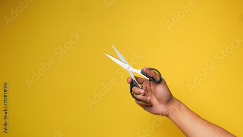Man's hand holding black scissors on a yellow background