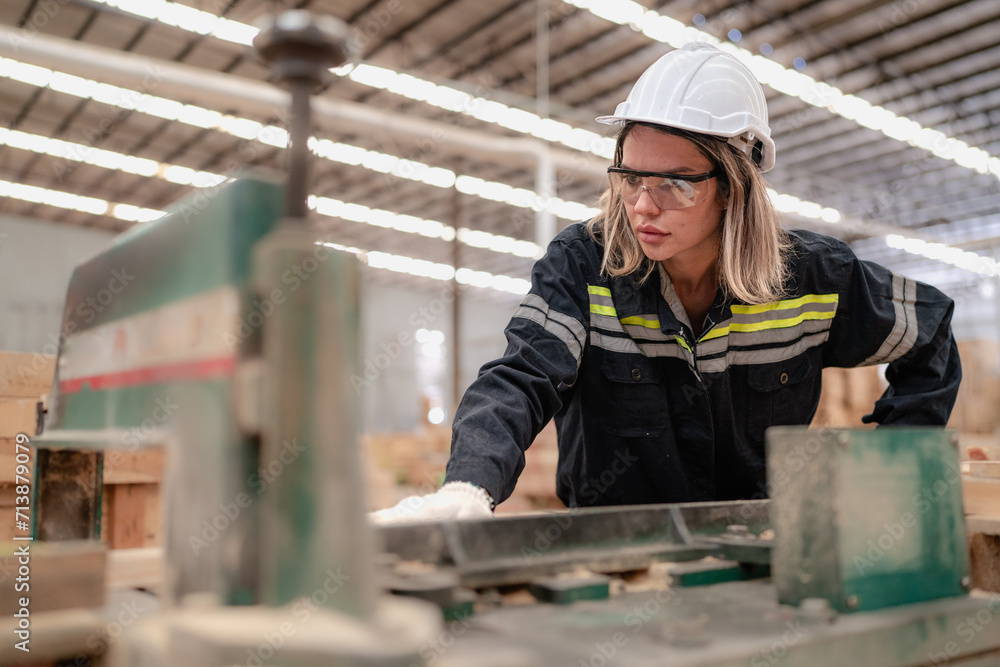 Confident female worker working in hardwood warehouse of wooden furniture factory checking stock. Busy skilled inspector in uniform hardhat examining plank pallet material for production facility. Confident female worker working in hardwood warehouse of wooden furniture factory checking stock. Busy skilled inspector in uniform hardhat examining plank pallet material for production facility.