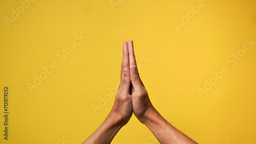 Men's hands praying and begging God for forgiveness on a yellow background