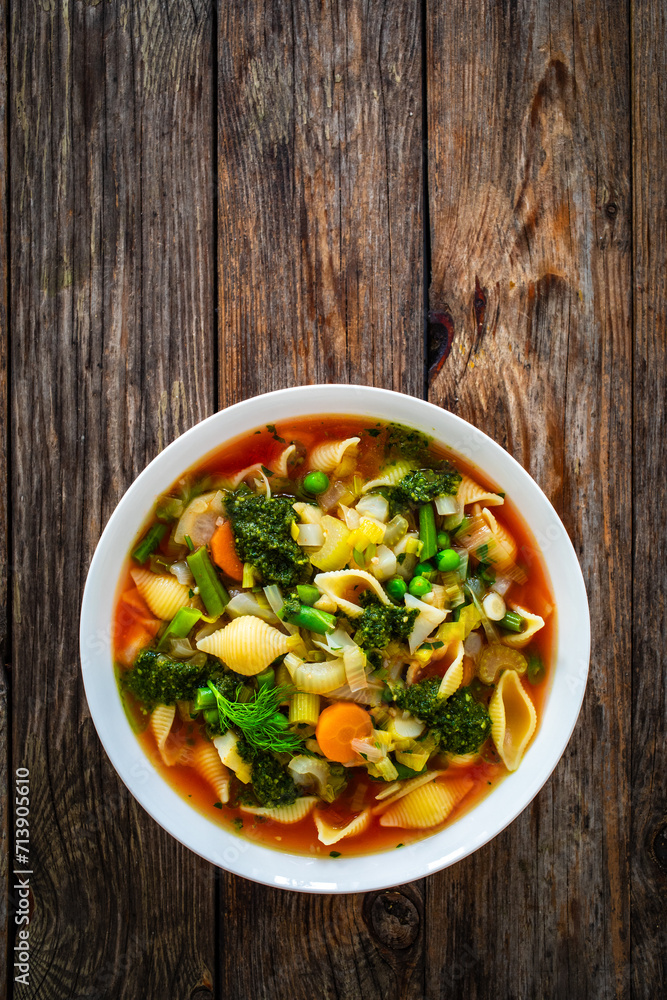 Pistou soup Nice - broth with basil pesto, noodles and vegetables on wooden background in white bowl Pistou soup Nice - broth with basil pesto, noodles and vegetables on wooden background in white bowl