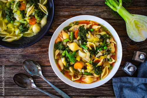 Pistou soup Nice - broth with basil pesto, noodles and vegetables on wooden background in white bowl photo