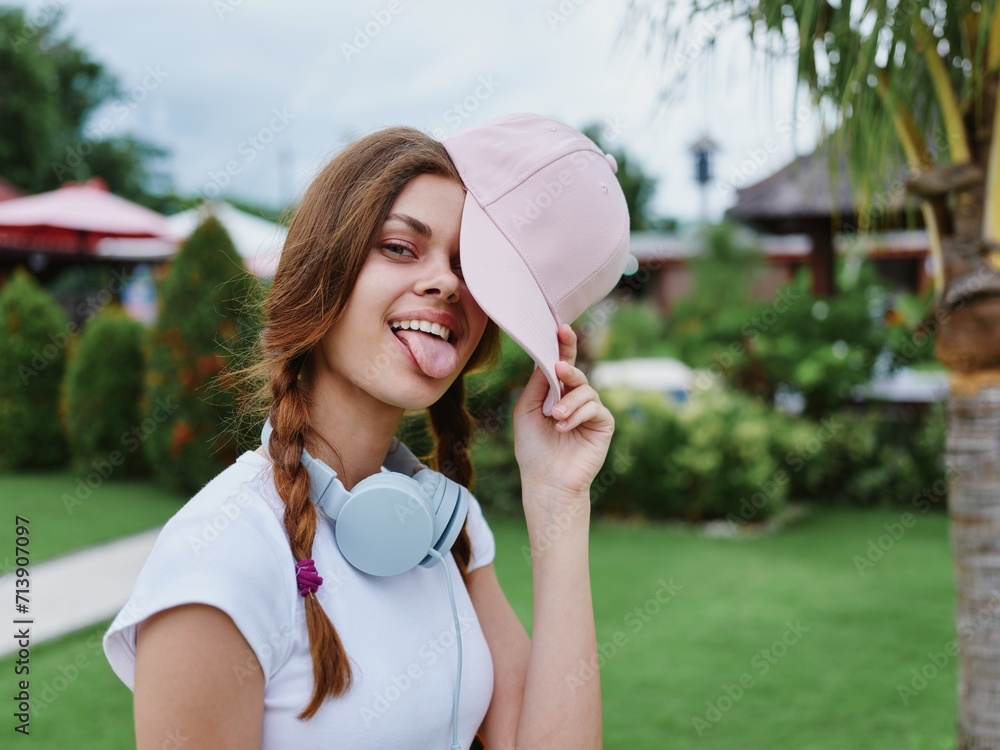 Fototapeta premium Teenage girl school in a pink cap with a backpack and headphones in a white T-shirt goes to school in college smile with teeth