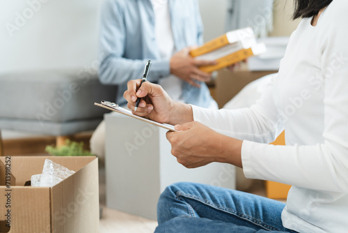 Happy woman checking stuff in cardboard box before sent to transportation company and moving to new location apartment. © Pormezz