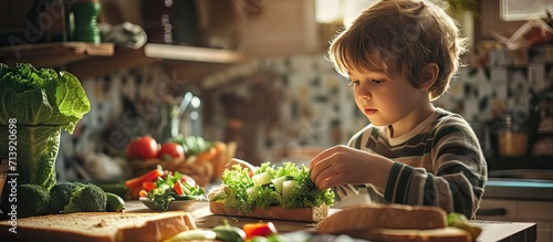 Cute little boy making vegetable sandwich with fresh ingredients he places lettuce on bread in kitchen at home. Creative Banner. Copyspace image photo