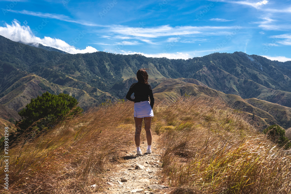 Woman hiking alone on a mountain path, surrounded by vast hills and a clear blue sky, evoking adventure and freedom. At San Nicolas, Pangasinan, part of the Cordillera mountains. Woman hiking alone on a mountain path, surrounded by vast hills and a clear blue sky, evoking adventure and freedom. At San Nicolas, Pangasinan, part of the Cordillera mountains.