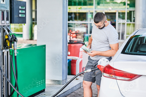 Concerned man looking if he has enough money to refuel his car. Young man needs to spend a lot of money to fill tank with gasoline. Fuel price crisis concept.