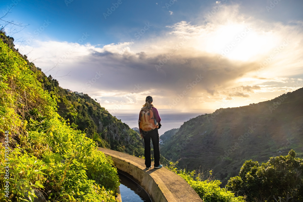 Tourist on Levada do Norte on the Portuguese island of Madeira. Levada irrigation canal. Hiking in Madeira. Narrow path next to the levada. Green mountains and ocean in background.