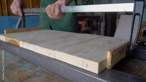 Male carpenter glues boards in a carpentry workshop. Manufacture of furniture boards and countertops. clamping wooden products with a clamp.