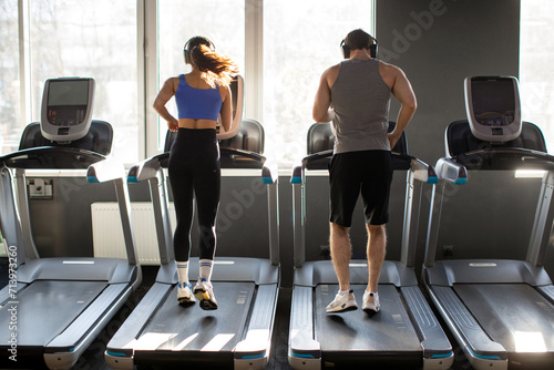Back view of active young couple running on treadmills, man and woman performing cardio workout in gym. Families practicing self-care photo