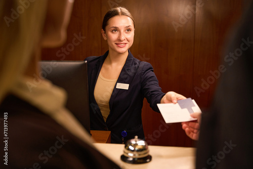 Smiling receptionist standing and giving keycard to hotel guest photo