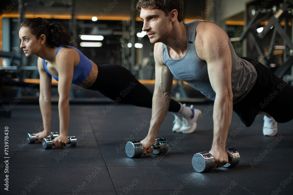 Sporty young caucasian couple doing plank or push-ups on weights, working out together in modern dark gym, closeup. Fitness, sports concept Sporty young caucasian couple doing plank or push-ups on weights, working out together in modern dark gym, closeup. Fitness, sports concept