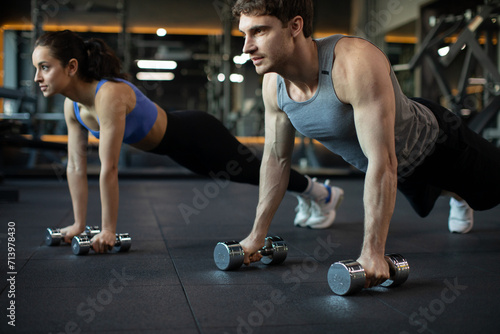 Sporty young caucasian couple doing plank or push-ups on weights, working out together in modern dark gym, closeup. Fitness, sports concept