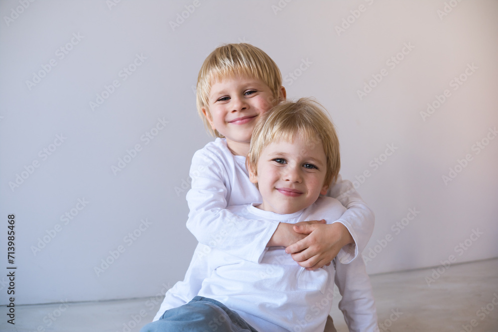 two little blonde smiling boys twins hugging, sitting on floor two little blonde smiling boys twins hugging, sitting on floor