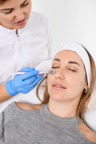 Cosmetologist s hands perform the procedure of electroporation of the area under the eyes in a beauty salon