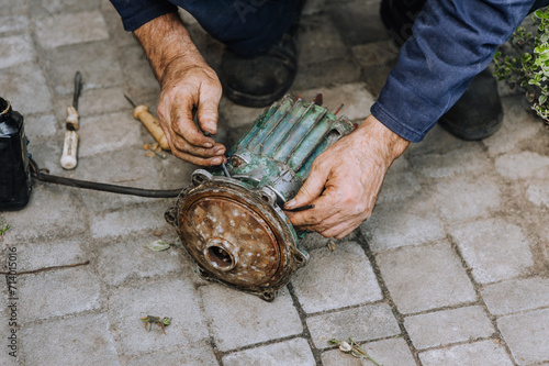 Elderly male professional worker, electrician, electromechanic repairs an old rusty electric motor in a workshop. Photography, close-up portrait, equipment repair. photo