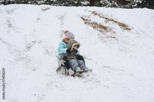 A little boy with a girl sister, happy children, a family ride while sitting on a sled, going down a hill in the snow in winter. Photography, portrait, childhood concept, lifestyle.