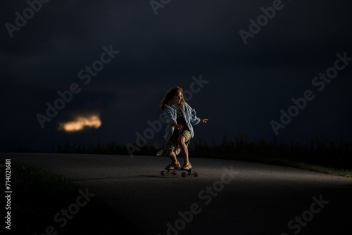 Young girl rides along the road standing on a longboard with her legs bent at the knees
